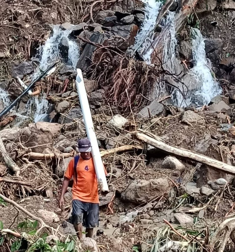 Seorang warga Desa Tolofuo melintasi area berbatu sambil membawa pipa air yang rusak, di tengah kondisi sumber air pancora yang hancur akibat banjir. Kerusakan ini memaksa warga berjuang secara mandiri demi memenuhi kebutuhan air bersih, sembari menanti perhatian dan penanganan dari pemerintah pascabencana. (Dok/Wrg)